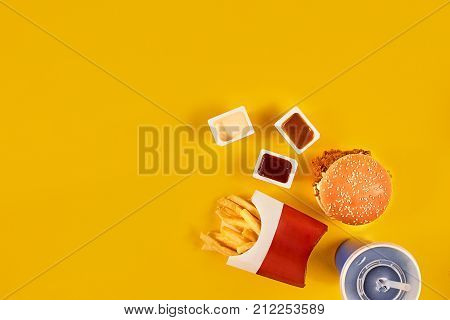 Fast food dish top view. Meat burger, potato chips and wedges. Take away composition. French fries, hamburger, mayonnaise and ketchup sauces on yellow background. Menu or receipt background. Top view. Copy space. Still life. Flat lay.