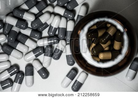 Looking down on Pill covered white counter with open pill bottle big pharma suicide deception black and white with color inside the bottle