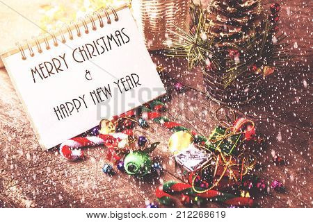 Merry christmas and Happynew year text on blank notebook with snow gift box daisy flower candy ball and cane pine decoration on vintage wooden background.