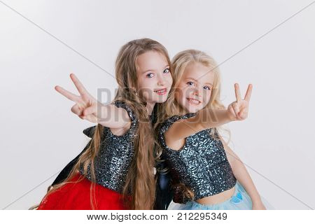 beautiful twq little girls with curly blonde hairstyles on the holiday party in dress with sequins and black jacket. Silver foil on the floor. Concept Celebration. Making peace by fingers