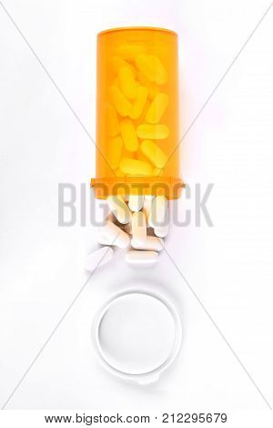 Medical pills spilling out from bottle. White medical tablets and pastic transparent pills container, top view.