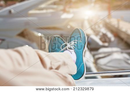 A pair of human legs in pants and bright blue topsiders on yacht background. Sunlight
