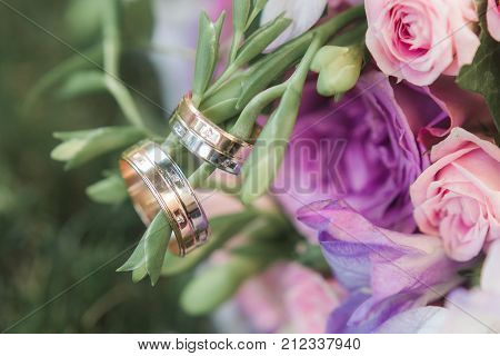 Gold wedding rings on bride's bouquet of purple roses. Macro close-up shot.