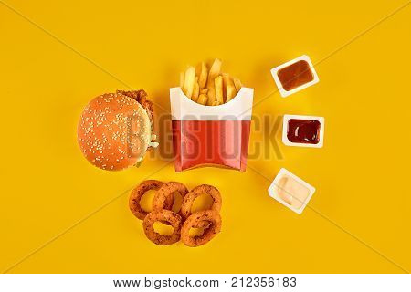 Fast food dish top view. Meat burger, potato chips and wedges. Take away composition. French fries, hamburger, mayonnaise and ketchup sauces on yellow background. Menu or receipt background. Top view. Copy space. Still life. Flat lay.