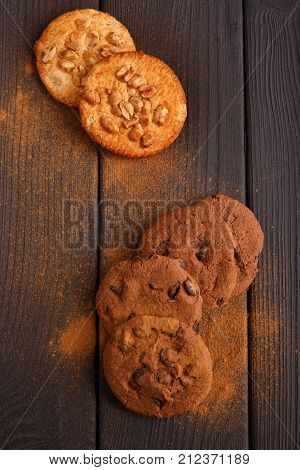 On the wooden table are a few oatmeal cookies and cookies with chocolate. A worn cinnamon on top. View from above. Inside.