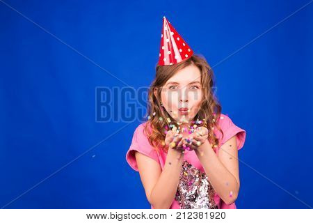 Close up portrait of attractive young woman blowing glitters. Caucasian Female model having fun over blue background
