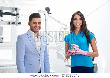 Cheerful handsome male patient smiling posing with his dentist at the clinic service friendly helpful specialist medicine staff healthcare appointment professionalism occupation job people.