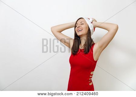Pretty caucasian young happy woman with healthy skin and charming smile wearing red dress and Christmas hat holding hands on head isolated on white background. Santa girl. New Year holiday 2018 concept