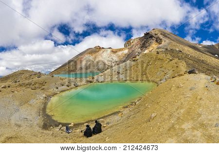 View at two hikers sitting in front beautiful Emerald lakes and watching Mount Ngauruhoe on Tongariro Crossing track, Tongariro National Park, New Zealand