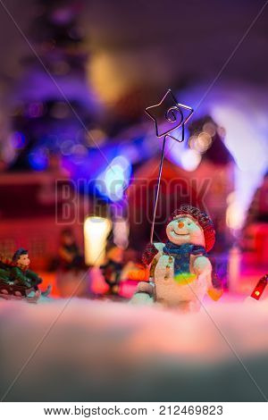 Kid playing on snow with snowman in colorful christmas village. holidays miniature scenery