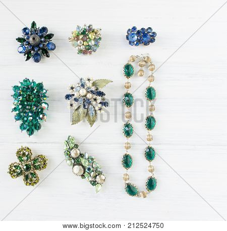 Woman's Jewelry. Vintage jewelry background. Beautiful bright rhinestone brooch necklace and earrings on white wood. Flat lay top view.