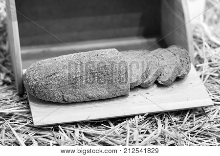fresh homemade loaf of baked rye bread with cut slices in wooden or wood breadbox or bin on straw with nobody