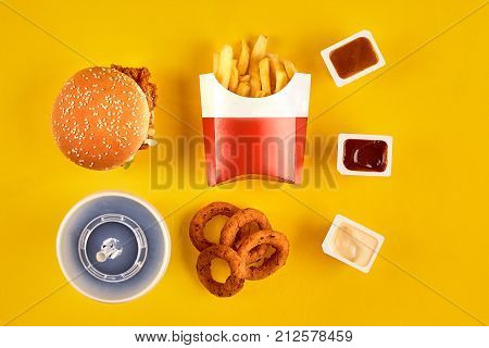 Fast food dish top view. Meat burger, potato chips and wedges. Take away composition. French fries, hamburger, mayonnaise and ketchup sauces on yellow background. Menu or receipt background. Top view. Copy space. Still life. Flat lay.