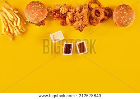 Fast food dish top view. Meat burger, potato chips and wedges. Take away composition. French fries, hamburger, mayonnaise and ketchup sauces on yellow background. Menu or receipt background. Top view. Copy space. Still life. Flat lay.