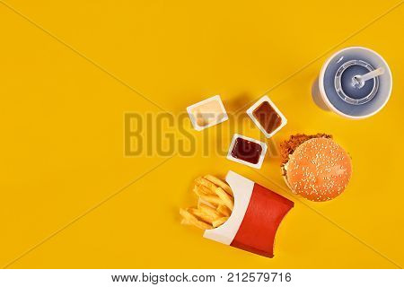 Fast food dish top view. Meat burger, potato chips and wedges. Take away composition. French fries, hamburger, mayonnaise and ketchup sauces on yellow background. Menu or receipt background. Top view. Copy space. Still life. Flat lay.