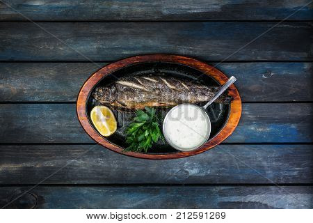 Frying pan with tasty trout fish on wooden background wine greens, sauce and lemon.