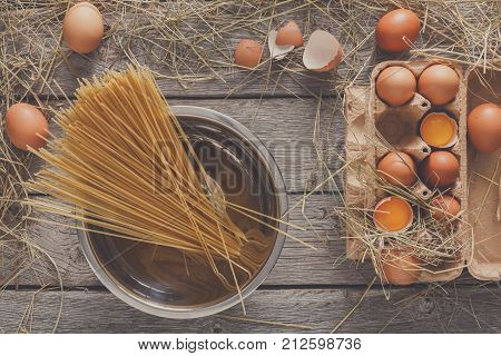Cooking background. Raw Vermicelli in pot and fresh chicken eggs in carton, top view on rustic wood background