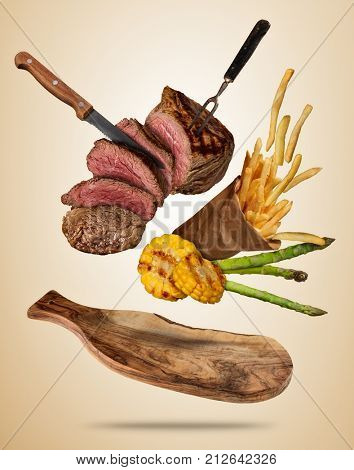 Flying beef steaks with grilled vegetable and french fries served on wooden cutting board. Concept of flying food. Separated on soft colored background. High resolution size