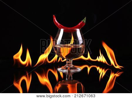 Stack of tequila on fire. Red burning pepper in a glass with alcohol also burns with fire in black background