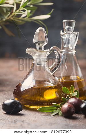 Olive oil in a glass bottle and olive branch on brown stone table