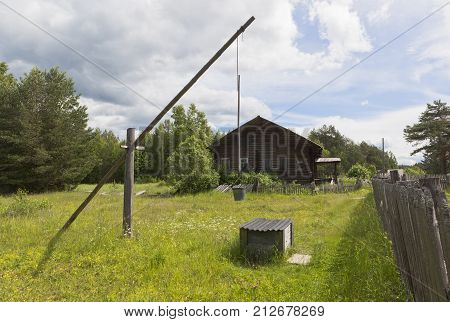 Water well on the background of an old house with boarded up windows. Russian remote