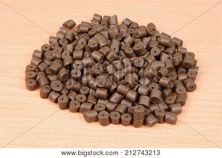 Brown pre-drilled halibut pellets for carp fishing isolated on wood background with soft shadow