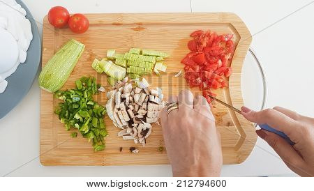 Top down view on wooden slate chopping board with hands cutting and slicing vegetables.