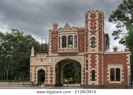 Parramatta Australia - March 24 2017: Red brick with beige trim castle-like George Street Gatehouse entrance to Domain park with Government House under heavy rainy sky. Green trees.