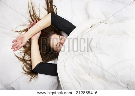 Young woman is lying in her bed with closed eyes, smiling under her blanket after a restful sleep. Lifestyle concept.