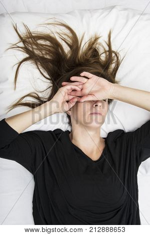 Depressed young woman is lying in her bed, covering her eyes.Sorrow concept.