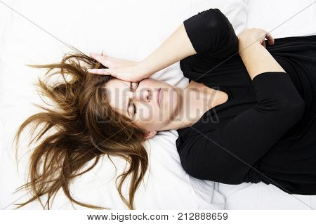 Young woman is lying in her bed with a painful expression on her face. Healthcare concept.
