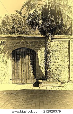 Stone wall with old gate decorated with palm tree in Tel Aviv. Israel historic warehouse on the line from Tel Aviv to Jerusalem. Vintage style toned picture