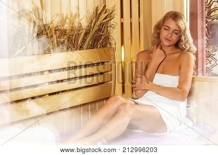Young beautiful woman relaxing in the Finnish sauna wrapped in towel