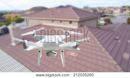 Unmanned Aircraft System (UAV) Quadcopter Drone In The Air Over House Inspecting the Roof.