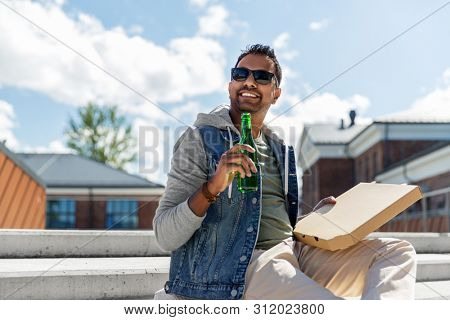 leisure, eating and fast food concept - indian man with takeaway pizza and drinking beer on roof top