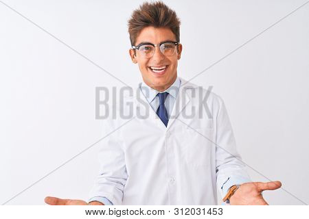 Young handsome sciencist man wearing glasses and coat over isolated white background smiling cheerful with open arms as friendly welcome, positive and confident greetings