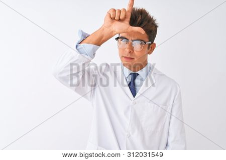 Young handsome sciencist man wearing glasses and coat over isolated white background making fun of people with fingers on forehead doing loser gesture mocking and insulting.