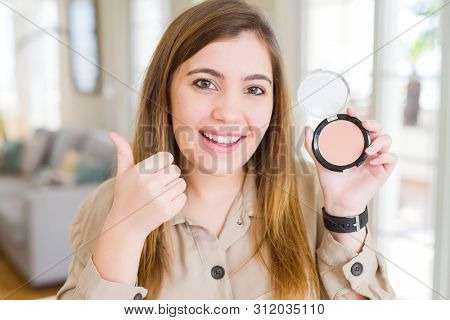 Beautiful young woman using make up cosmetics applying powder happy with big smile doing ok sign, thumb up with fingers, excellent sign