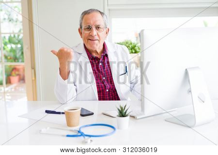 Handsome senior doctor man doing research using laptop looking for a cure at the clinic pointing and showing with thumb up to the side with happy face smiling