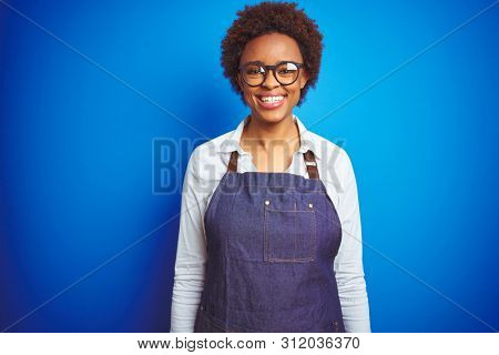 Young african american woman shop owner wearing business apron over blue background with a happy and cool smile on face. Lucky person.