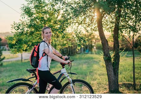Active Life. Sporty Young Blonde Girl In Sports Clothes With A Backpack Rides A Bike And Smiles At T