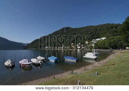 Beautiful View Of Many Boats Lined At The Shore Of Caslano Village Lakeside. This Village Is A Famou