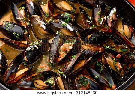 Mussel Shells In Cream Sauce In A Black Cauldron On A Dark Wooden Background, Decorated With Vegetab