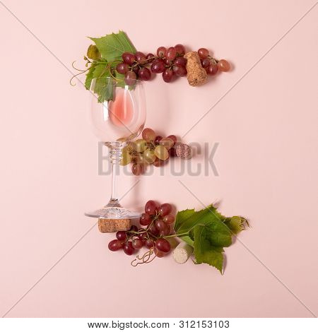 Alphabet. Letter E Made Of Wineglasses With Rose And White Wine, Grapes, Leaves And Corks Lying On P