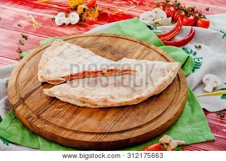 Half Of The Baked Calzone - Closed Type Of Pizza That Is Folded In Half, On A Round Wooden Board On 
