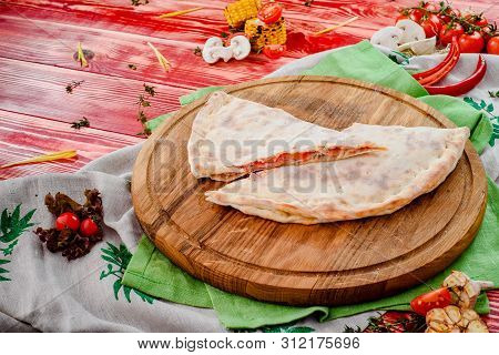 Half Of The Baked Calzone - Closed Type Of Pizza That Is Folded In Half, On A Round Wooden Board On 