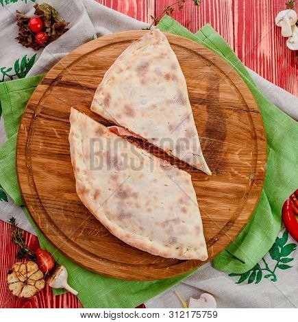 Half Of The Baked Calzone - Closed Type Of Pizza That Is Folded In Half, On A Round Wooden Board On 
