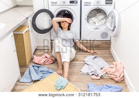 Sad Woman Sitting In Laudry Room With A Pile Of Dirty Clothes