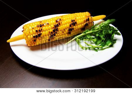 Grilled Corncob With Corncob Holder, Corncob Picker And Arugula Salad On A Plate