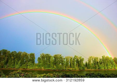 Rain Storm Including A Rainbow Above A Temperate Forest Besides The Willamette River Taken Near Port